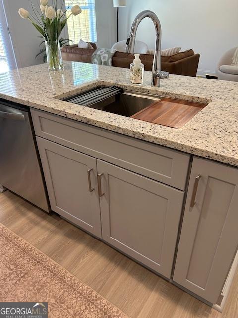 322 Heron St, Ball Ground, GA 30107 - kitchen view of stainless steel dishwasher, light wood-style floors, gray cabinetry, and light stone counters