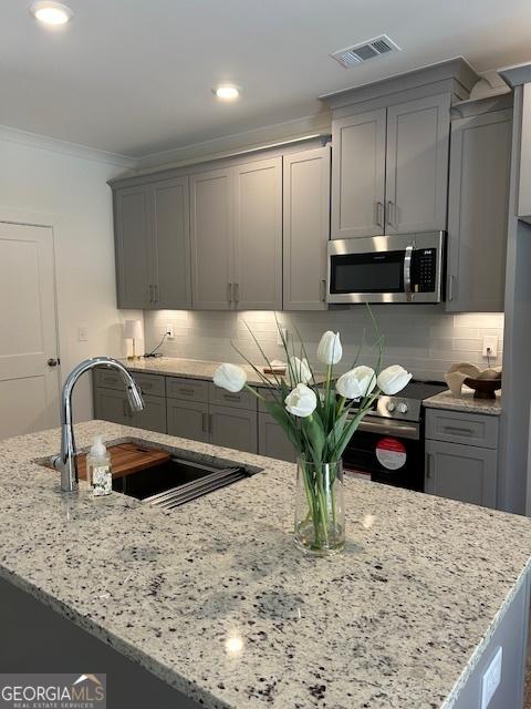 322 Heron St, Ball Ground, GA 30107 - kitchen with appliances with stainless steel finishes, gray cabinets, light stone countertops, crown molding, and decorative backsplash