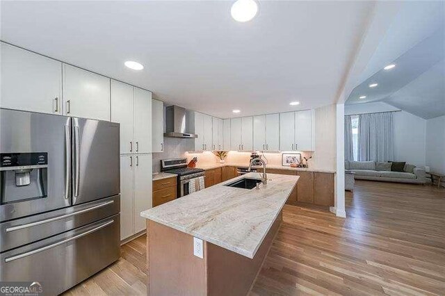 503 Rising Dr, Woodstock, GA 30189 - kitchen featuring appliances with stainless steel finishes, wall chimney exhaust hood, light wood-style flooring, white cabinetry, and vaulted ceiling