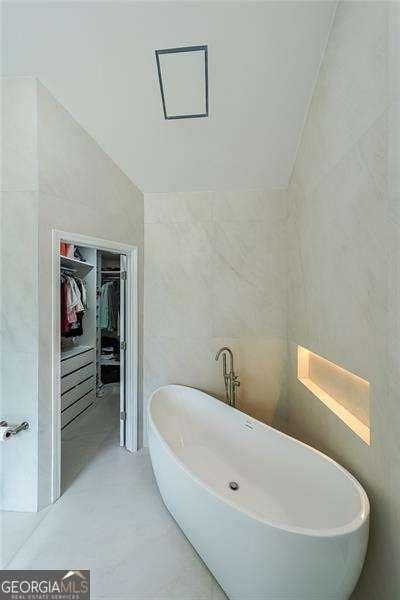 503 Rising Dr, Woodstock, GA 30189 - bathroom featuring a spacious closet, tile walls, a freestanding tub, and lofted ceiling