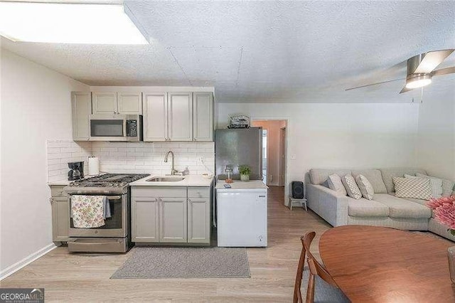 503 Rising Dr, Woodstock, GA 30189 - kitchen featuring appliances with stainless steel finishes, gray cabinetry, backsplash, light wood-type flooring, and a textured ceiling