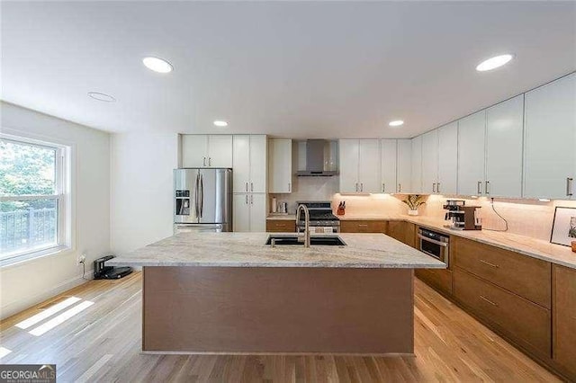 503 Rising Dr, Woodstock, GA 30189 - kitchen with stainless steel appliances, wall chimney exhaust hood, light wood-style floors, light stone counters, and a center island with sink