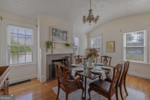 204 S Jefferson Ave, Eatonton, GA 31024 - dining room with light wood-style floors, a chandelier, a brick fireplace, lofted ceiling, and a textured wall