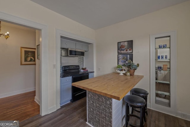 204 S Jefferson Ave, Eatonton, GA 31024 - kitchen with black range with electric stovetop, wood counters, stainless steel microwave, dark wood-style floors, and a breakfast bar area