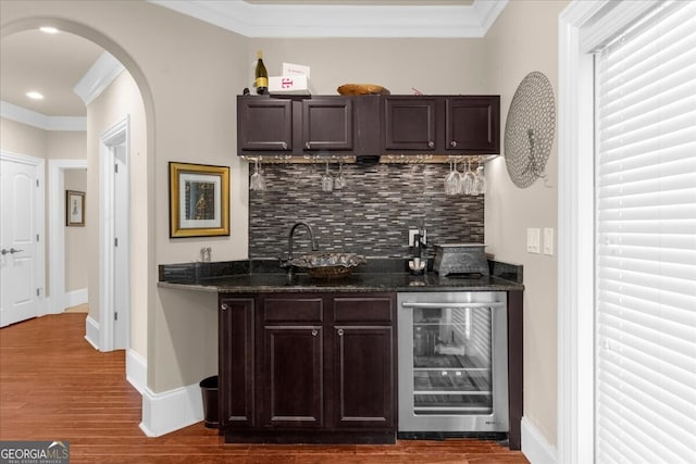 932 Shadowford Fls, Lithonia, GA 30058 - indoor wet bar featuring wine cooler, decorative backsplash, ornamental molding, dark wood finished floors, and arched walkways