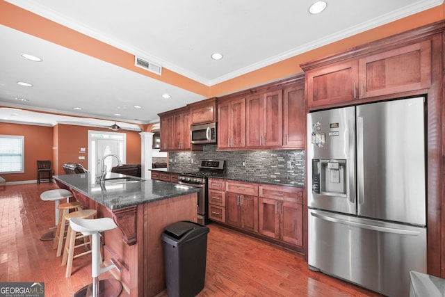 2670 Trotters Pointe Dr, Snellville, GA 30039 - kitchen featuring appliances with stainless steel finishes, crown molding, tasteful backsplash, a kitchen bar, and an island with sink