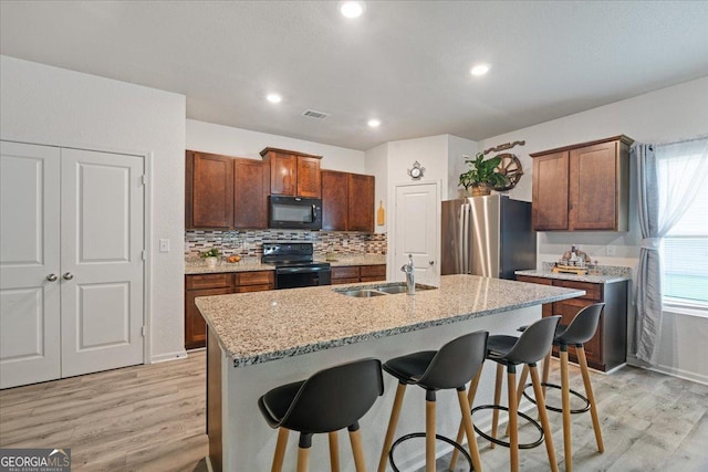 255 Morning Dr, Athens, GA 30606 - kitchen featuring black appliances, light wood finished floors, a kitchen breakfast bar, an island with sink, and light stone countertops