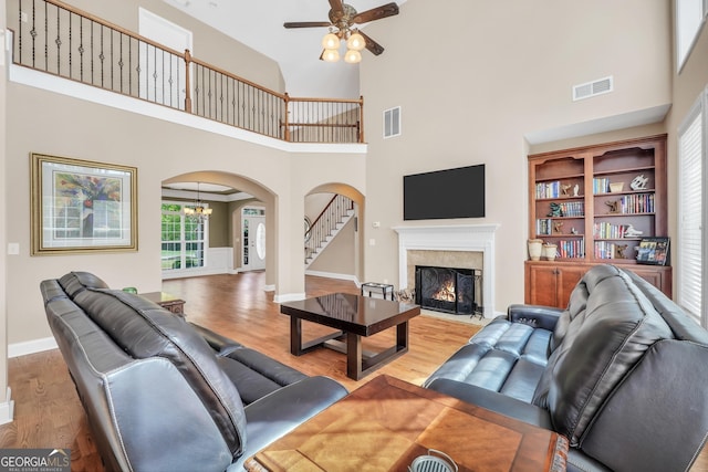 204 Carmell Ct, Mcdonough, GA 30252 - living room featuring arched walkways, a towering ceiling, a ceiling fan, light wood finished floors, and a premium fireplace