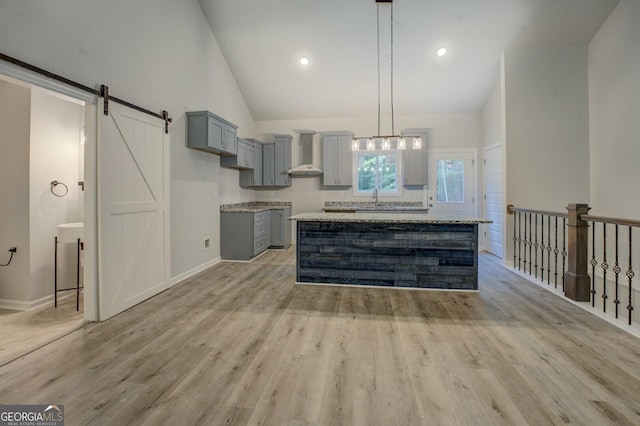 48 Bluejay Ct, Monticello, GA 31064 - kitchen with gray cabinets, wall chimney range hood, light wood-style floors, a barn door, and high vaulted ceiling