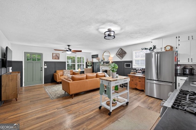 1724 Cedar Grove Church Rd, Winder, GA 30680 - living area featuring a textured ceiling, wood finished floors, a ceiling fan, a fireplace, and wainscoting