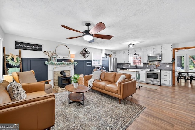 1724 Cedar Grove Church Rd, Winder, GA 30680 - living room featuring a textured ceiling, a ceiling fan, light wood-type flooring, a wood stove, and a wainscoted wall