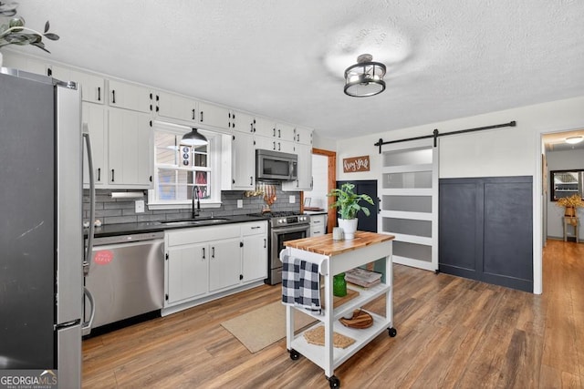 1724 Cedar Grove Church Rd, Winder, GA 30680 - kitchen with a barn door, stainless steel appliances, wood finished floors, tasteful backsplash, and a textured ceiling