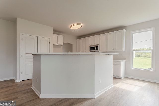 70 Trinity Ln, Covington, GA 30016 - kitchen featuring stainless steel microwave, light wood-type flooring, white cabinetry, and light countertops