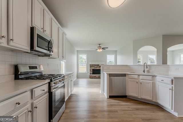 70 Trinity Ln, Covington, GA 30016 - kitchen featuring appliances with stainless steel finishes, a ceiling fan, a stone fireplace, light wood-style floors, and decorative backsplash