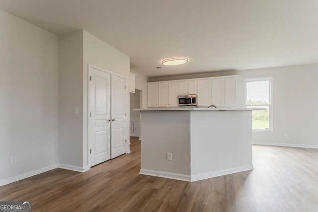 70 Trinity Ln, Covington, GA 30016 - kitchen with stainless steel microwave, wood finished floors, white cabinetry, light countertops, and a kitchen island with sink