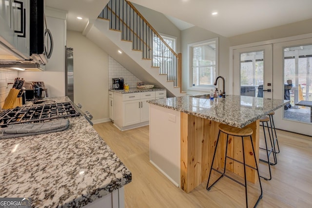 480 Mitchell Rd, Covington, GA 30014 - kitchen with light wood-style floors, backsplash, a kitchen breakfast bar, light stone countertops, and white cabinetry