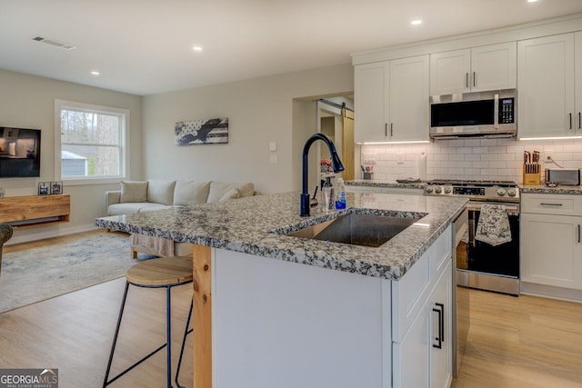 480 Mitchell Rd, Covington, GA 30014 - kitchen with appliances with stainless steel finishes, light wood-type flooring, light stone counters, a kitchen island with sink, and recessed lighting