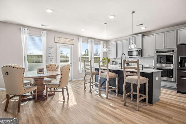 1049 Bodega Loop, Locust Grove, GA 30248 - kitchen featuring stainless steel appliances, light wood-style flooring, light countertops, a center island with sink, and a breakfast bar area