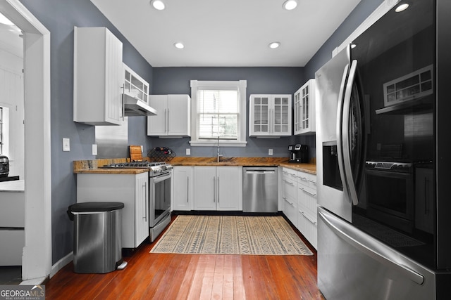 303 W 39th St, Savannah, GA 31405 - kitchen featuring appliances with stainless steel finishes, under cabinet range hood, glass insert cabinets, white cabinets, and wood finished floors