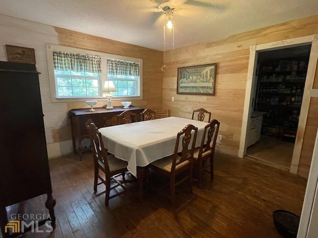 dining room featuring wooden walls, ceiling fan, a textured ceiling, and dark hardwood / wood-style flooring