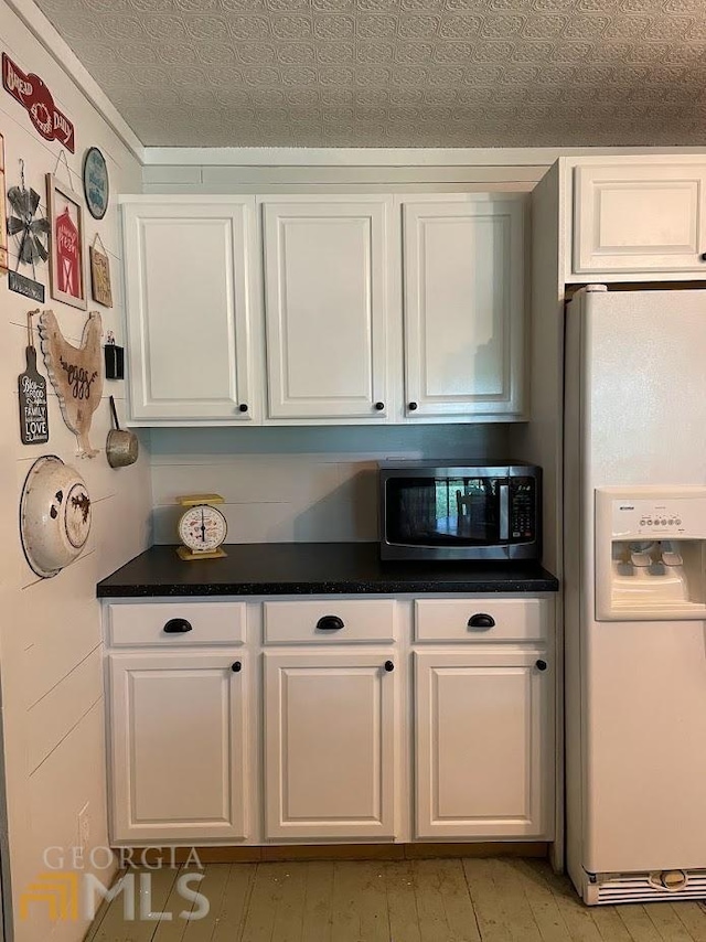 kitchen featuring white fridge with ice dispenser, white cabinetry, and a textured ceiling