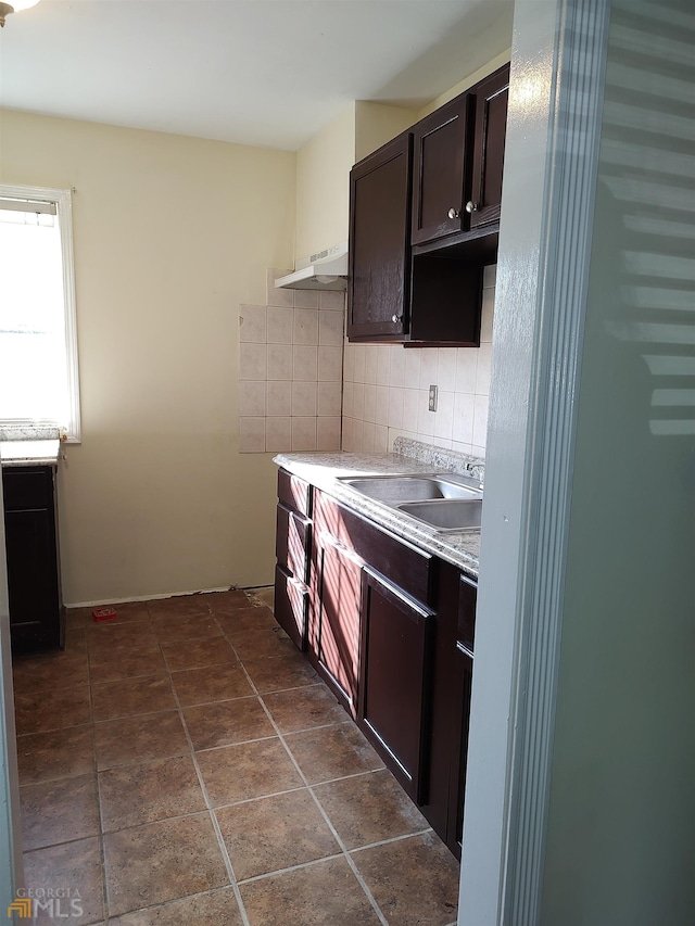 kitchen with sink, dark tile flooring, custom range hood, tasteful backsplash, and dark brown cabinetry