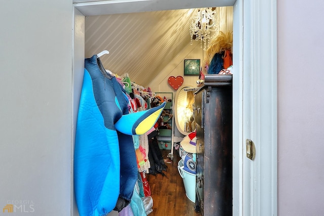 walk in closet featuring a notable chandelier, dark wood-type flooring, and vaulted ceiling