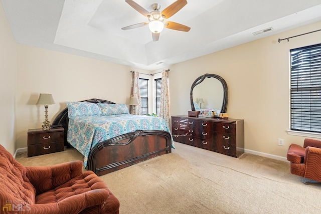 carpeted bedroom with ceiling fan and a tray ceiling