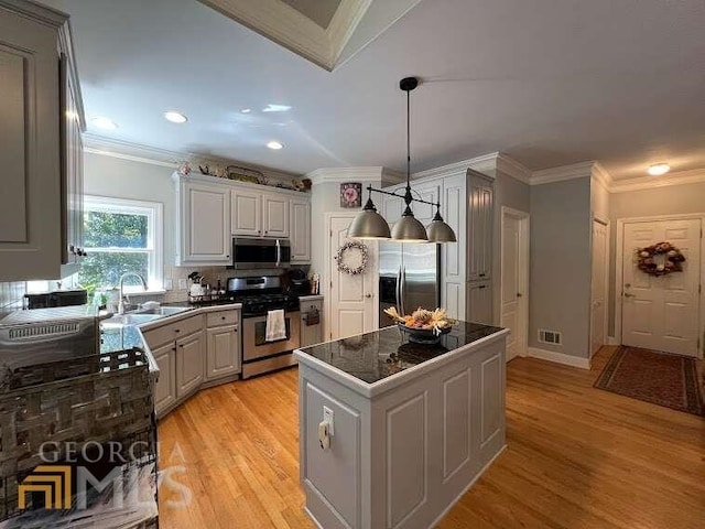 kitchen featuring ornamental molding, light wood-type flooring, stainless steel appliances, and pendant lighting