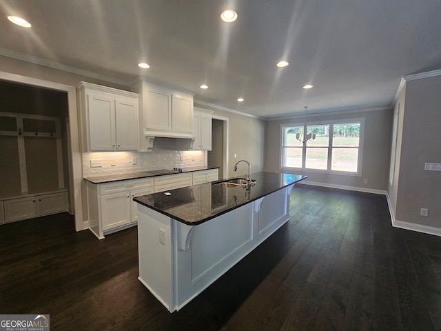 kitchen with white cabinets, a kitchen breakfast bar, a kitchen island with sink, dark wood-type flooring, and crown molding