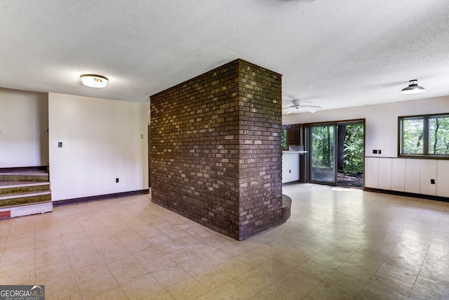 unfurnished room featuring ceiling fan, a textured ceiling, light tile flooring, and brick wall