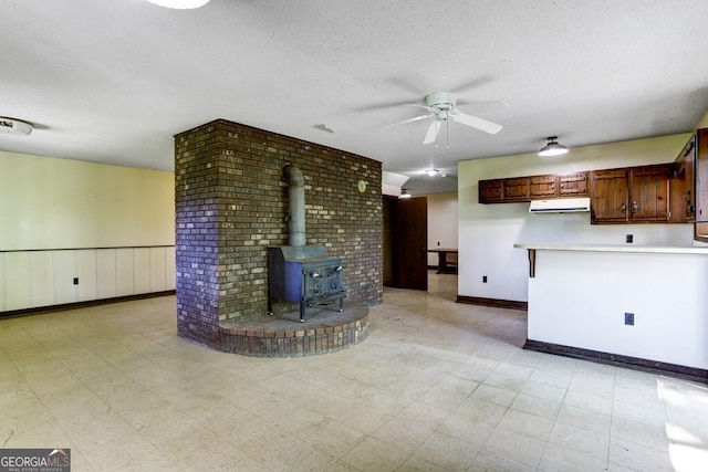 unfurnished living room featuring a textured ceiling, brick wall, a wood stove, light tile flooring, and ceiling fan