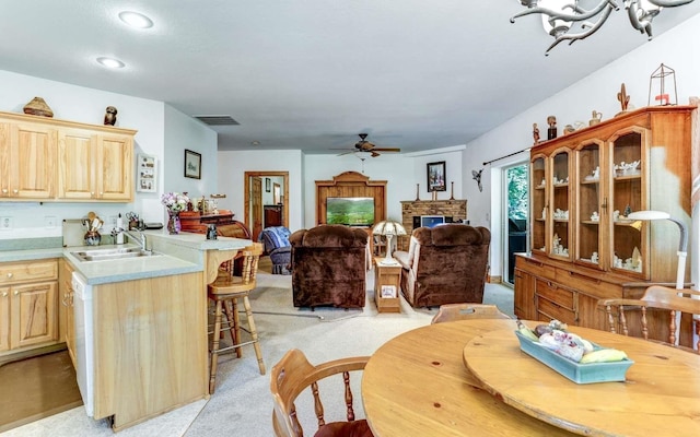 kitchen with ceiling fan with notable chandelier, light brown cabinets, sink, light colored carpet, and a stone fireplace