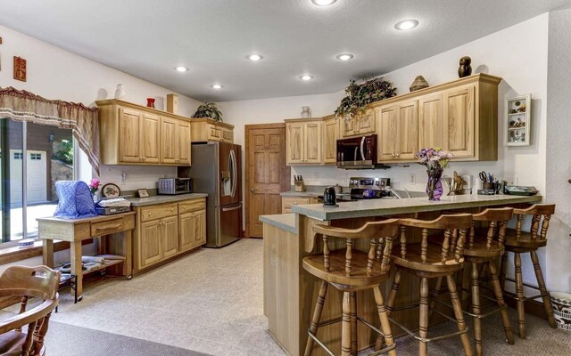 kitchen featuring light brown cabinetry, stainless steel appliances, light tile floors, and a kitchen breakfast bar