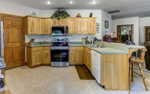 kitchen with appliances with stainless steel finishes, light tile flooring, a breakfast bar, sink, and kitchen peninsula