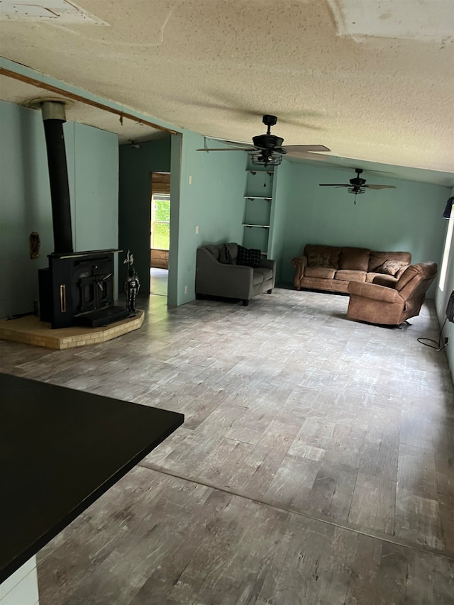 unfurnished living room featuring ceiling fan, a textured ceiling, a wood stove, and wood-type flooring