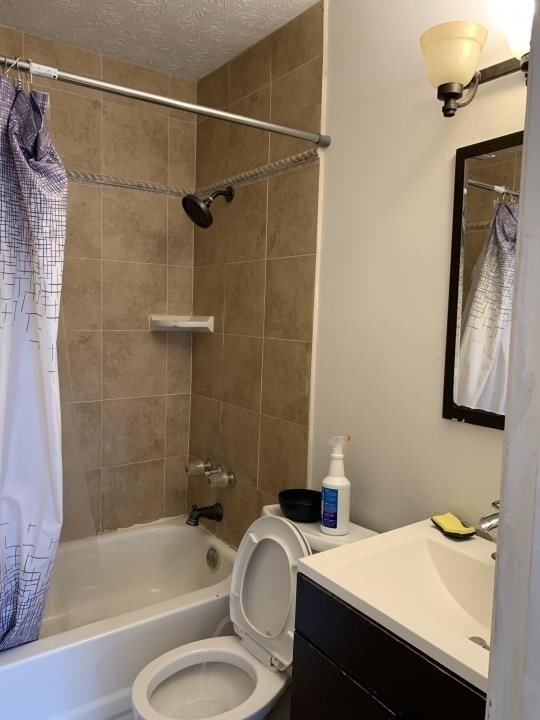 full bathroom with shower / bath combination with curtain, oversized vanity, toilet, and a textured ceiling