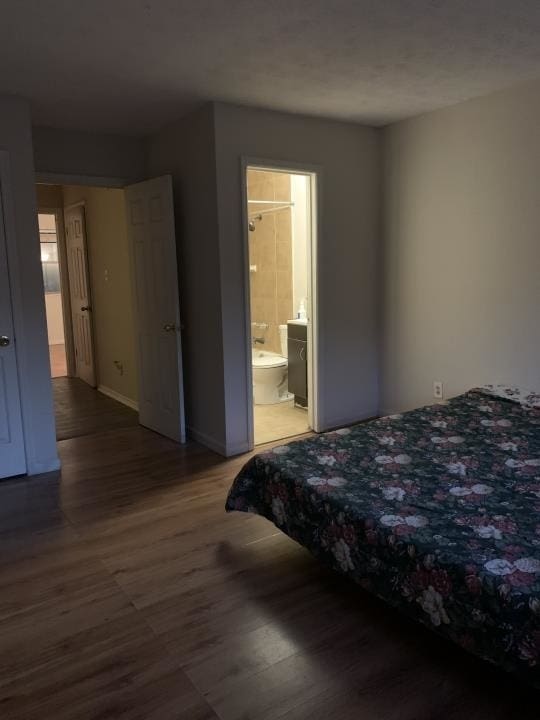 bedroom with ensuite bathroom and dark wood-type flooring