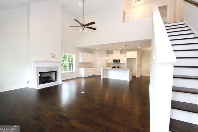 unfurnished living room with ceiling fan, dark hardwood / wood-style floors, a towering ceiling, and a high end fireplace