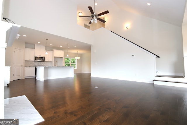 unfurnished living room featuring ceiling fan, high vaulted ceiling, and dark wood-type flooring