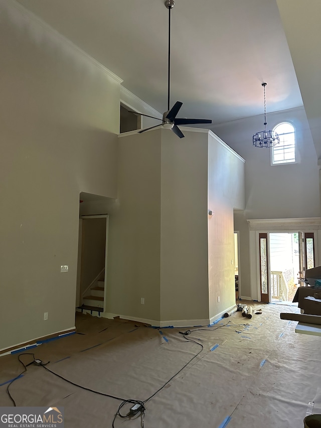 unfurnished living room featuring ceiling fan with notable chandelier, a wealth of natural light, and a high ceiling