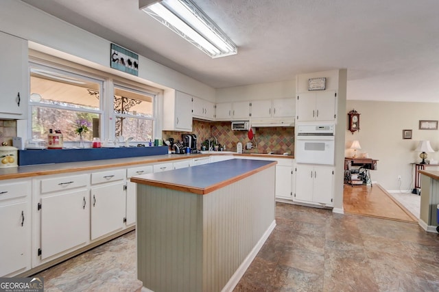 kitchen featuring white cabinetry, decorative backsplash, a center island, and oven