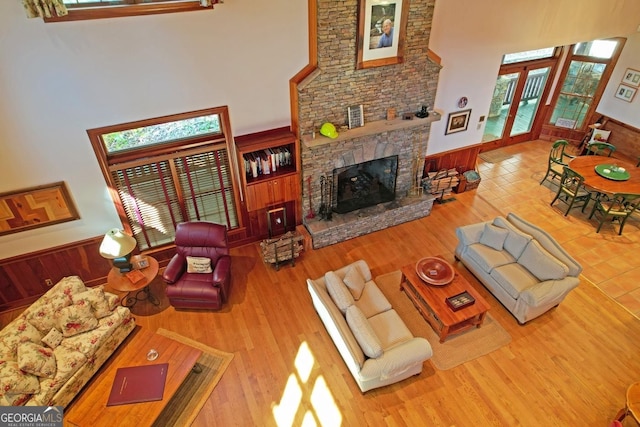 living room with a stone fireplace, a healthy amount of sunlight, light hardwood / wood-style floors, and a towering ceiling