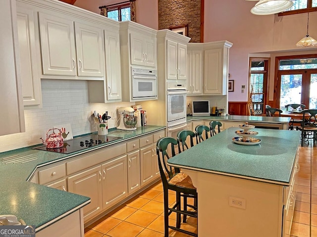 kitchen featuring light tile floors, a kitchen island, black electric cooktop, a high ceiling, and tasteful backsplash