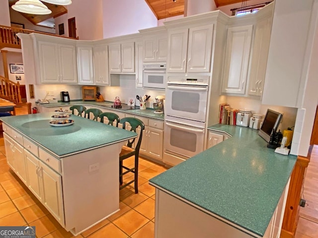 kitchen with a kitchen island, a breakfast bar area, white cabinetry, light tile floors, and double oven