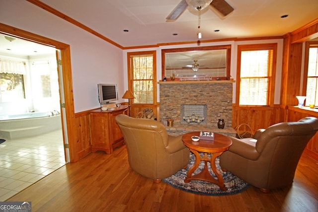 living room with ceiling fan, crown molding, tile flooring, and a stone fireplace