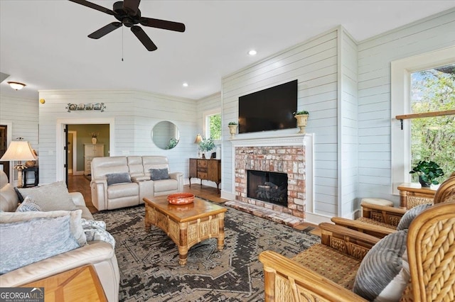 living room with ceiling fan, wooden walls, dark hardwood / wood-style floors, and a brick fireplace