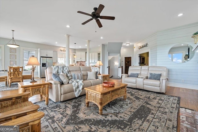 living room featuring dark hardwood / wood-style floors, decorative columns, wooden walls, and ceiling fan