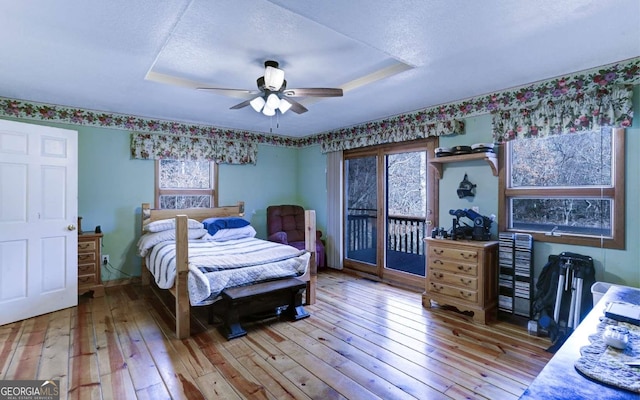 bedroom featuring light hardwood / wood-style flooring, a tray ceiling, ceiling fan, and multiple windows