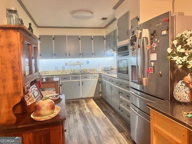 kitchen with appliances with stainless steel finishes, gray cabinetry, ornamental molding, sink, and dark hardwood / wood-style floors